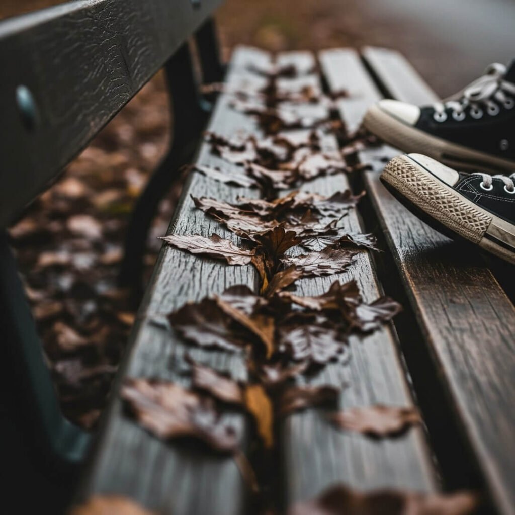 A crooked photo of a park bench with wet leaves and sneakers