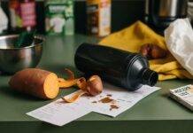 Men’s Nutrition: Why Eating Right is the Secret to Staying Strong in Your 30s & 40s A slightly blurry shot of a chaotic kitchen counter with a half-peeled sweet potato, a dented protein shaker, a coffee-stained grocery list, and a flip-flop peeking out from underneath.