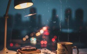 Why Mental Health Education is Critical for Our Future—A Deep Dive A blurry, photorealistic image of a messy desk with a doodle-filled notebook, a chipped "Keep Going" mug, and a city skyline visible through a streaky window.