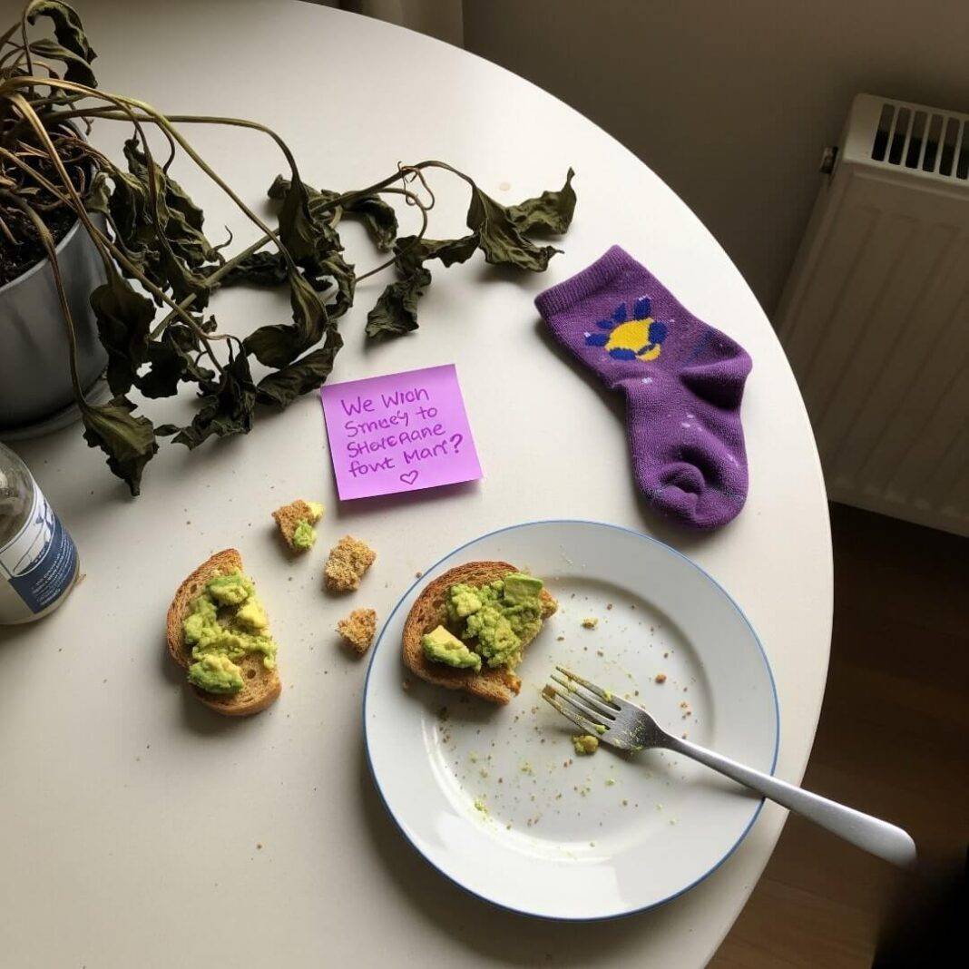 A high-angle, slightly shaky shot of a kitchen table with avocado toast crumbs, a sticky note, and that purple sock, with soft morning light and a wilting plant in the corner. A high-angle, slightly shaky shot of a kitchen table with avocado toast crumbs, a sticky note, and that purple sock, with soft morning light and a wilting plant in the corner.