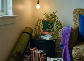 Holistic Health and Wellness: 10 Steps to Start Living Your Best Life A dimly lit corner of a cluttered apartment features a rolled-up, coffee-stained yoga mat, stacks of self-help books, a drooping fern, and a bright purple polka-dot sock hanging from an armchair.