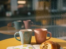 Mental Health Coaching: 7 Benefits You Didn’t Know About A blurry phone photo of a coffee shop table with chipped mugs, a stained notebook with smiley doodles, a crumbling croissant, and a rainy window.