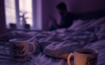 Sleep Disorder Advocacy: Helping Millions Sleep Better A blurry, low-angle shot of a kitchen at 4 a.m. with a burnt popcorn bag, a firefly near a flickering lamp, and a person slumped over a table.