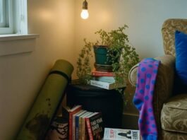 Holistic Health and Wellness: 10 Steps to Start Living Your Best Life A dimly lit corner of a cluttered apartment features a rolled-up, coffee-stained yoga mat, stacks of self-help books, a drooping fern, and a bright purple polka-dot sock hanging from an armchair.