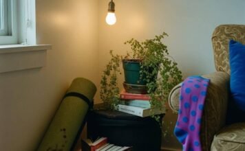 Holistic Health and Wellness: 10 Steps to Start Living Your Best Life A dimly lit corner of a cluttered apartment features a rolled-up, coffee-stained yoga mat, stacks of self-help books, a drooping fern, and a bright purple polka-dot sock hanging from an armchair.