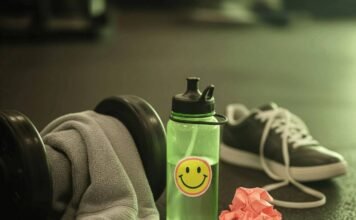 Why Hiring a Fitness Coach Near You Will Jumpstart Your Goals A sweaty gym towel on a dumbbell, a water bottle with a sticker, a crumpled workout plan, and a sneaker on a gym floor